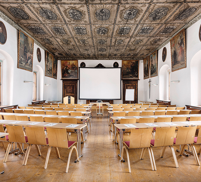 Konferenzbestuhlung im historischen Klostersaal Traunkirchen mit Leinwand und kunstvoll verzierter Kassettendecke.