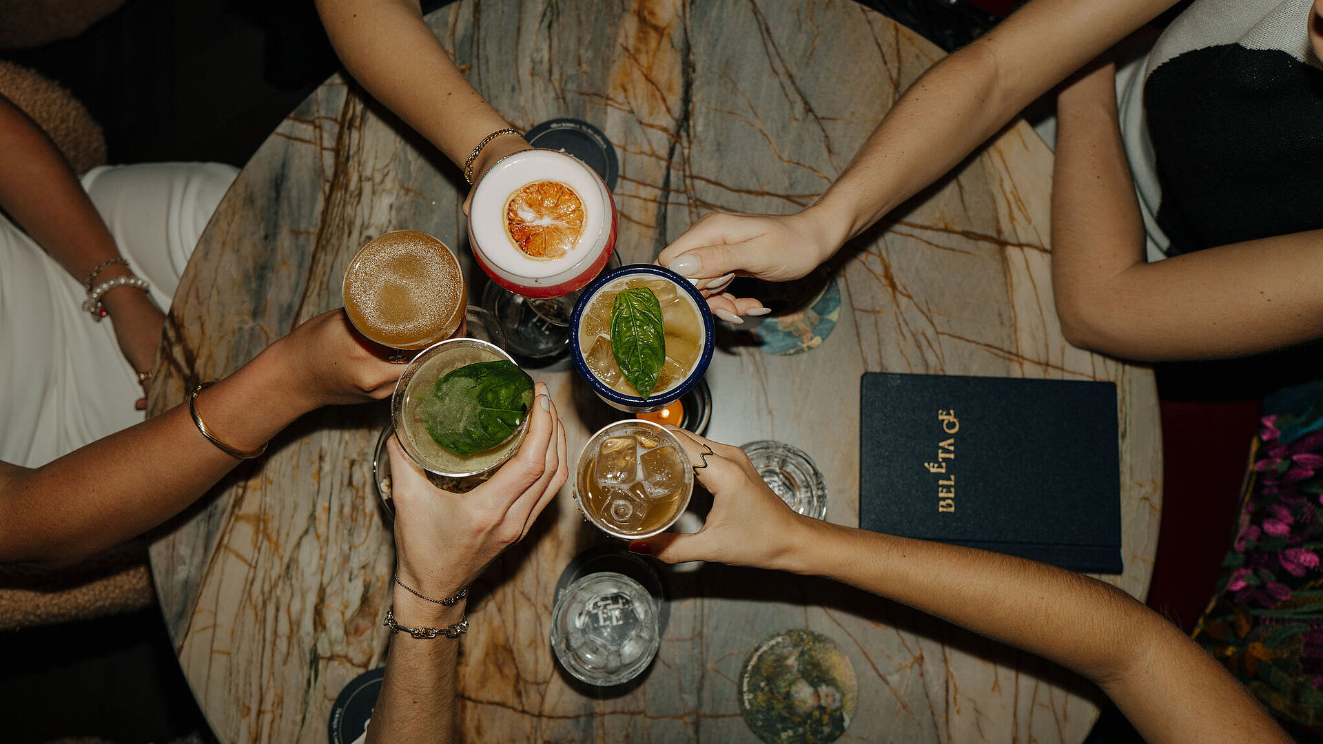 Freunde sitzen an einem runden Tisch und genießen Cocktails in einer geselligen Atmosphäre im Restaurant Beletage