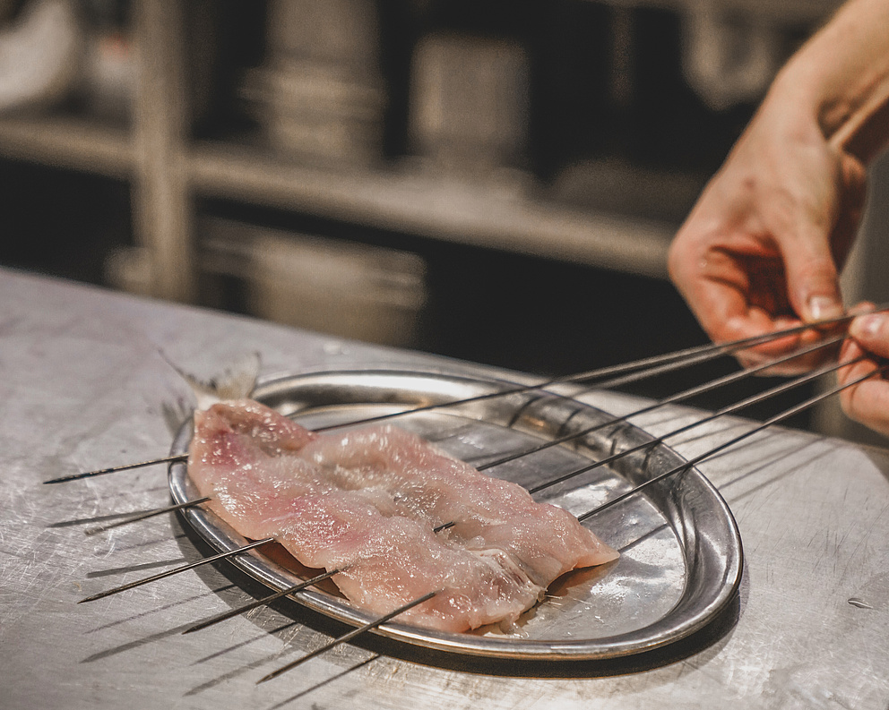 Kleine rohe Fischfilets auf Metallspießen in der Restaurantküche