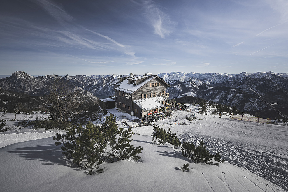 Kranabethhütte im Winter, umgeben von verschneiten Bergen, mit Skipiste im Vordergrund