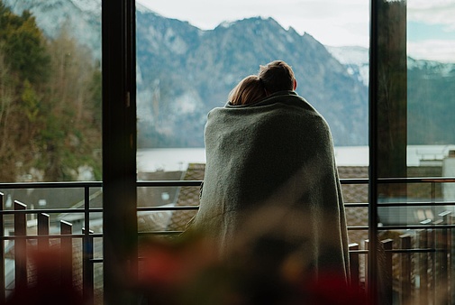 Paar in Decke gehüllt, das vom Zimmer aus den Blick auf Berge und See genießt.