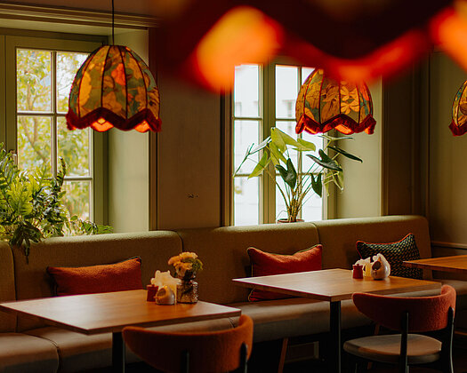Gemütlicher Restaurantbereich mit braunen Tischen und bunten Lampenschirmen in herbstlichen, warmen Tönen.