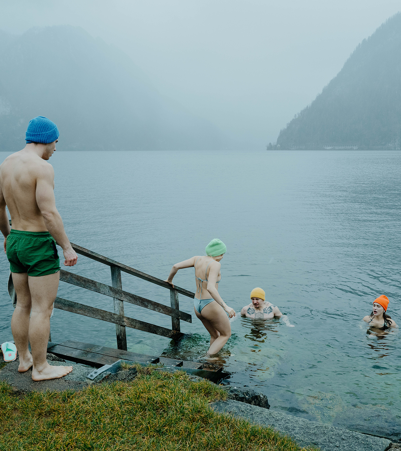 Gäste beim Eisbaden im Traunsee – einige bereits im Wasser, zwei wagen gerade den Einstieg. Winterliche Atmosphäre mit Nebel und Kälte