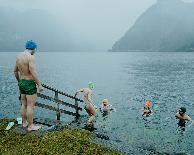 Gäste beim Eisbaden im Traunsee – einige bereits im Wasser, zwei wagen gerade den Einstieg. Winterliche Atmosphäre mit Nebel und Kälte