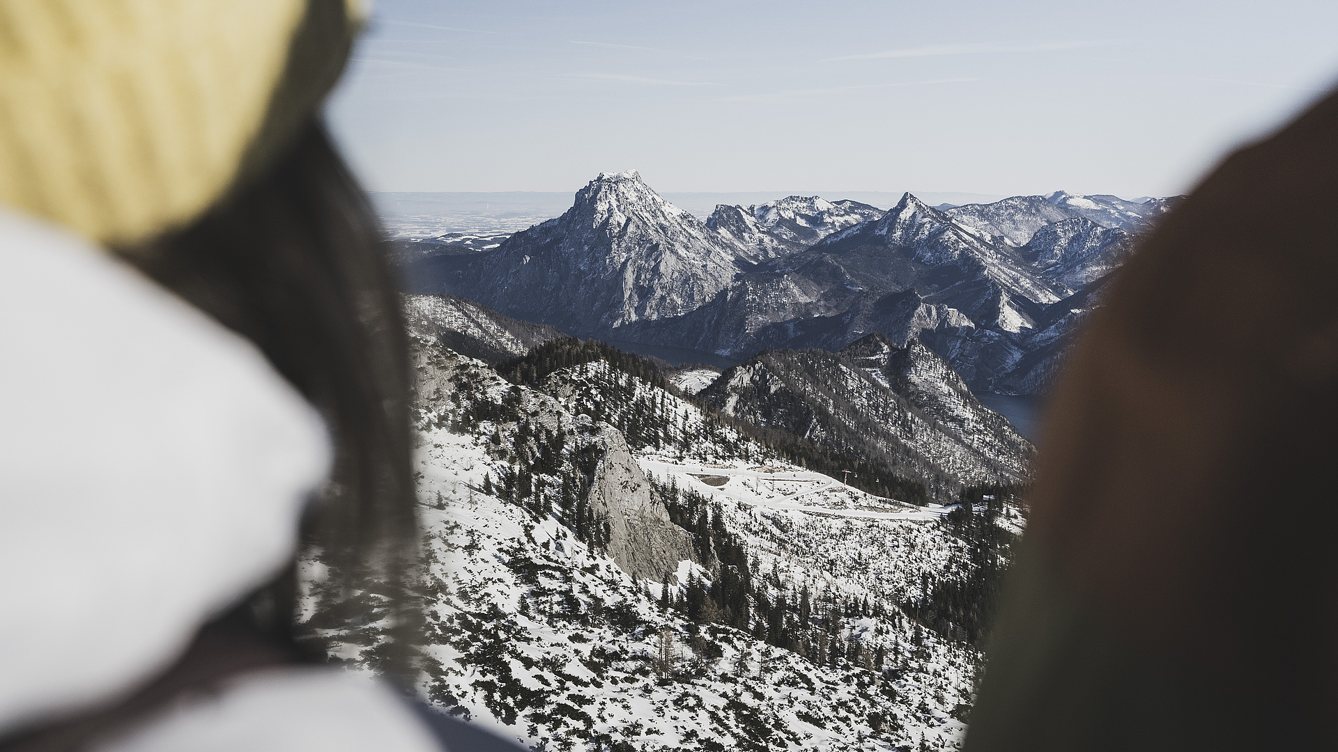 Frau in Skijacke und Mütze von hinten, die die schneebedeckte Berglandschaft im Winter betrachtet.