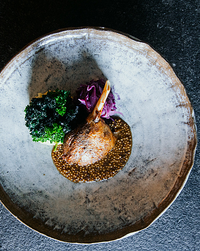 Entenkeule mit krosser Haut, winterlichen Aromen und Wintersalat auf marmoriertem Teller.