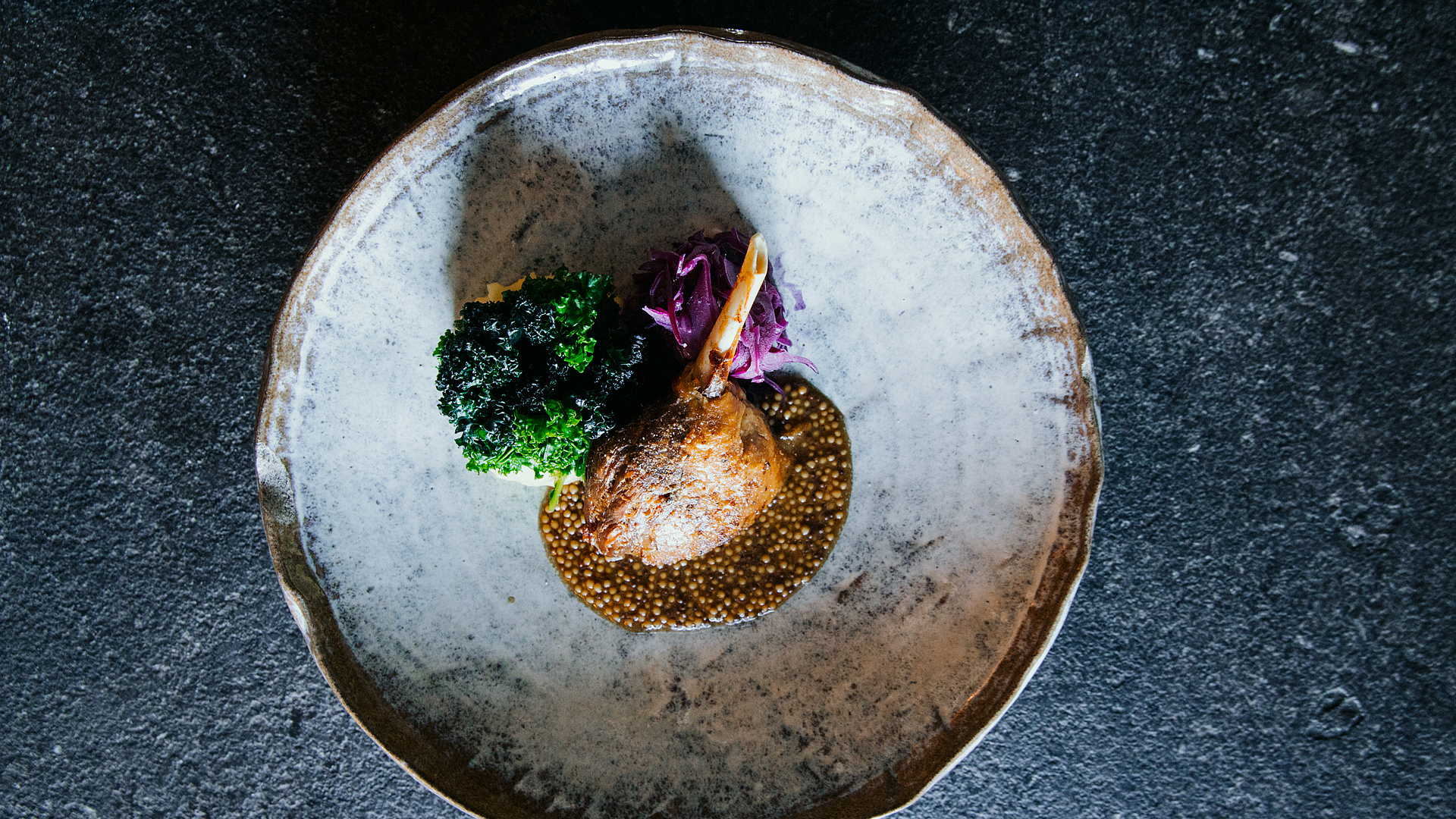 Entenkeule mit krosser Haut, winterlichen Aromen und Wintersalat auf marmoriertem Teller.