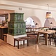 Innenansicht des Restaurants Poststube mit großen, hellen Holztischen, einem Kachelofen mit grünen Fliesen und hellem Holzboden