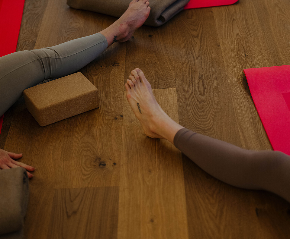 Beine verschiedener Teilnehmer auf dem Holzboden während einer Yogasession