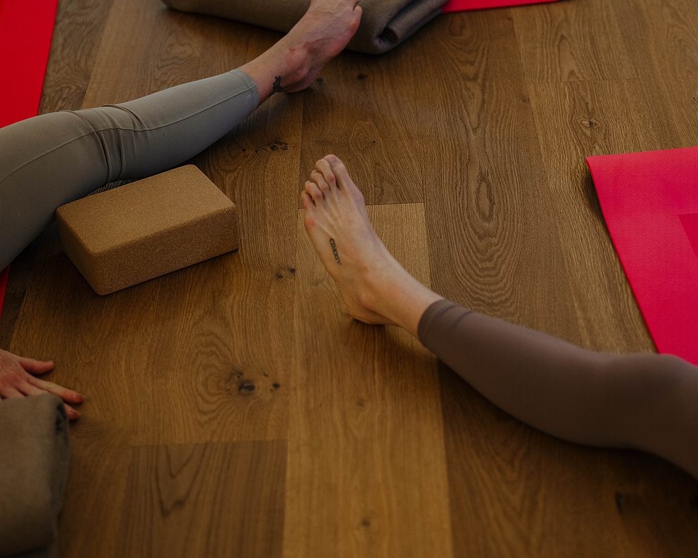 Beine verschiedener Teilnehmer auf dem Holzboden während einer Yogasession