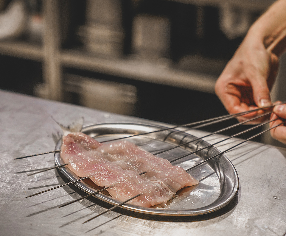 Kleine rohe Fischfilets auf Metallspießen in der Restaurantküche