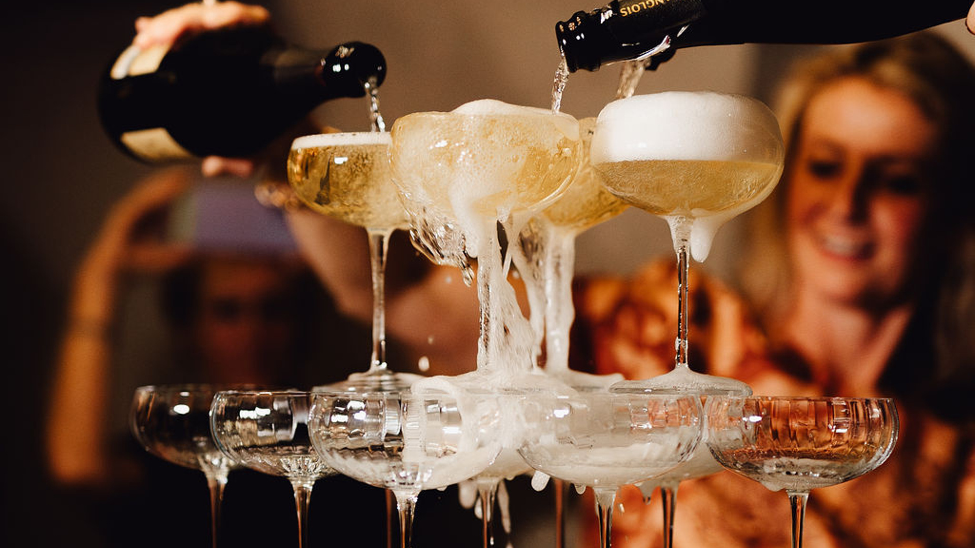 Gläserturm mit Champagner, der von oben eingegossen wird, im Hintergrund Partygäste.