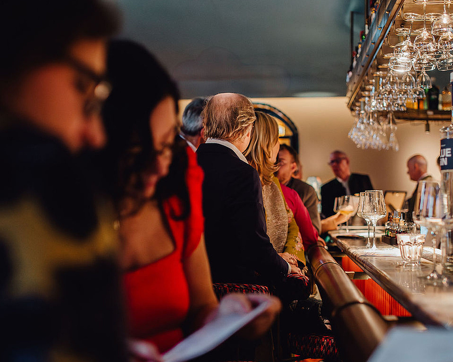 Viele elegant gekleidete Personen sitzen an der Bar in der Beletage und genießen ihre Getränke.
