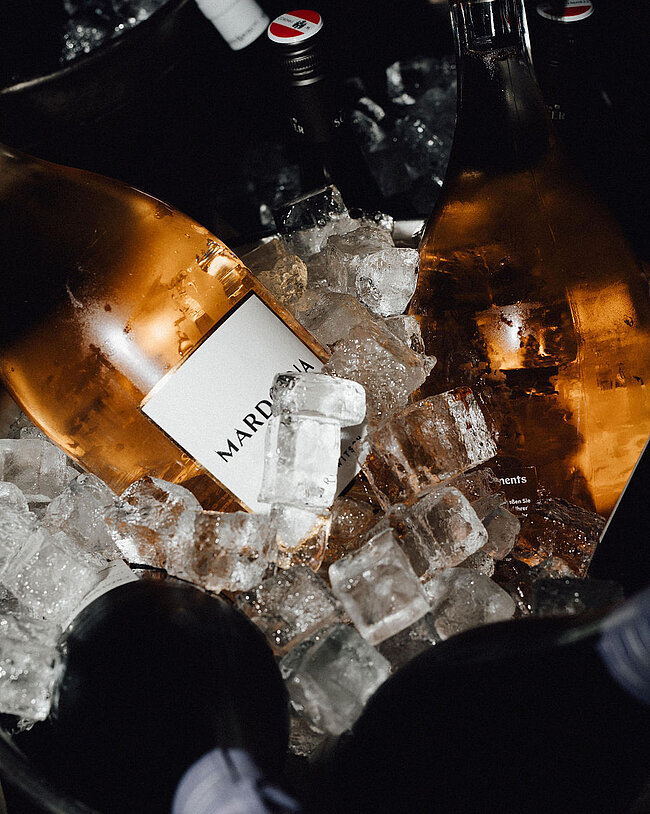 Unterschiedliche Wein- und Sektflaschen in einem Eiskübel mit Eiswürfeln, ideal für eine festliche Veranstaltung.
