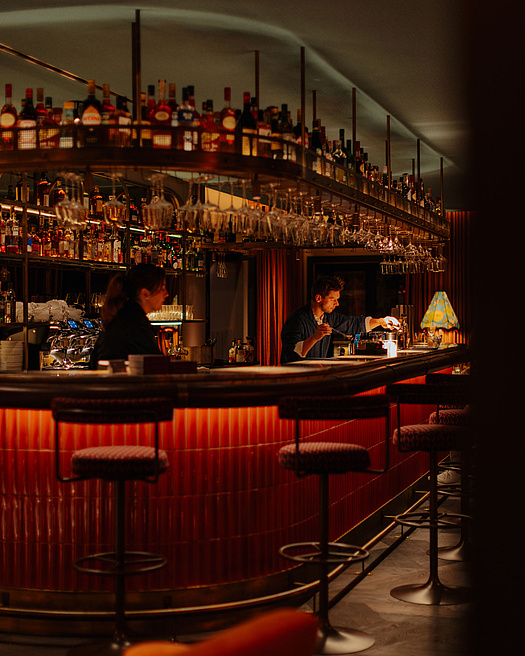 Der Barbereich mit gemütlichen Barstühlen, einer gut bestückten Bar und einem Barkeeper, der Getränke zubereitet