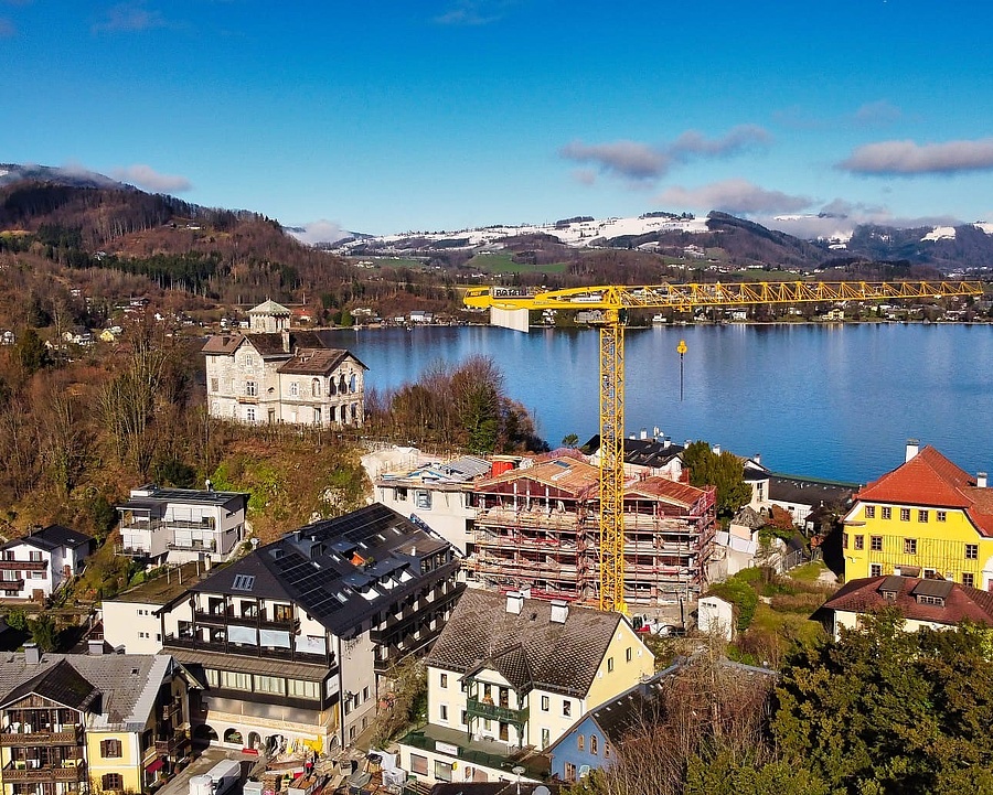 Drohnenaufnahme von Traunkirchen im Winter mit Baustelle des neuen Hotelzubaus, See und Berge im Hintergrund.