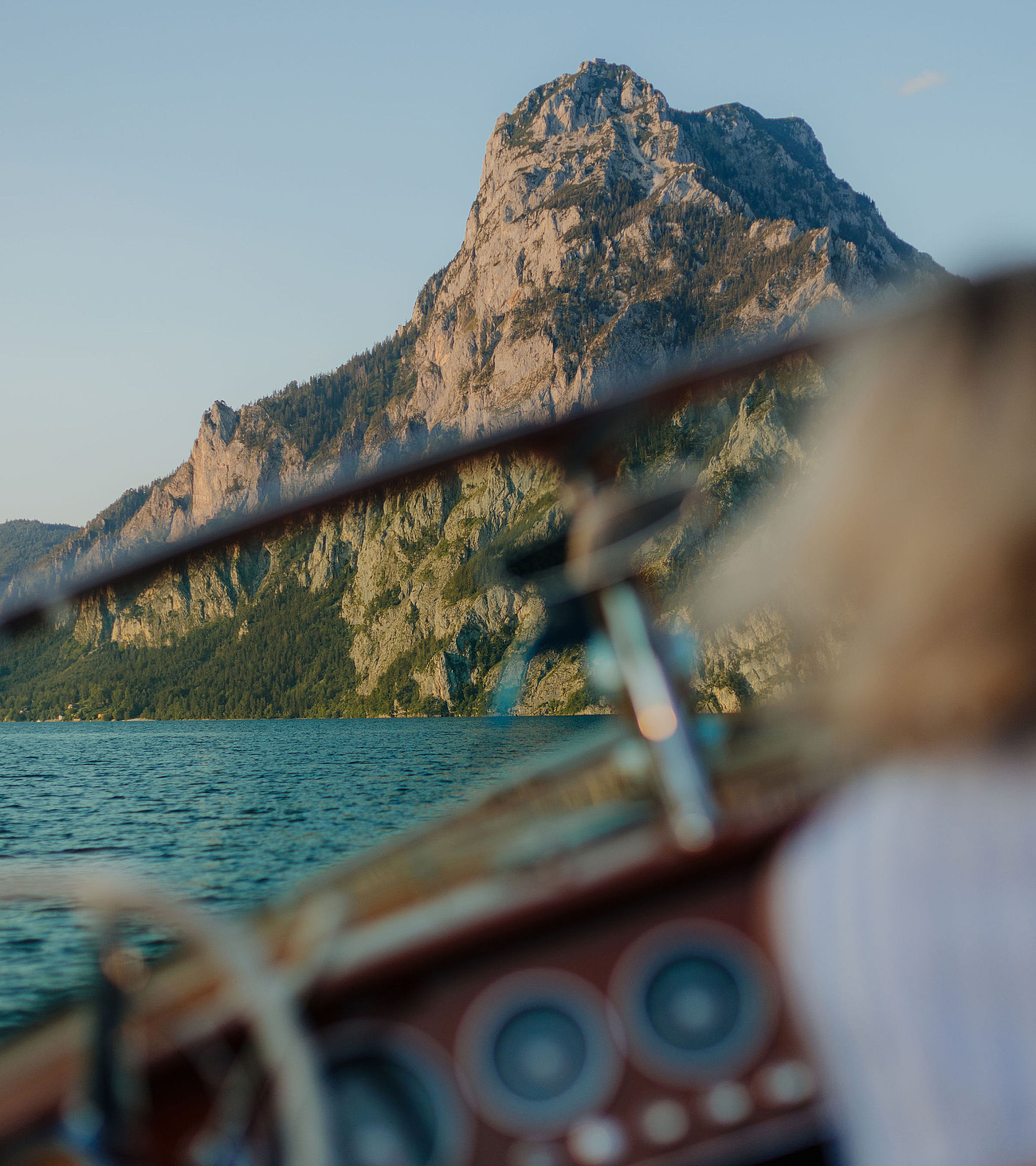 Unscharfe Frau in Boot im Vordergrund, scharfer Traunsee und Traunstein im Hintergrund, blauer Himmel, Sommer.