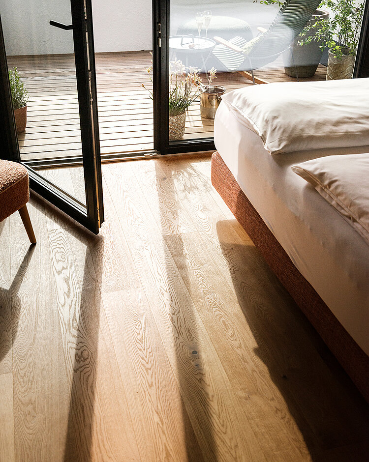 Offene Balkontür mit Blick auf den Balkon, Holzboden und frisch bezogenes Bett im Hotelzimmer.