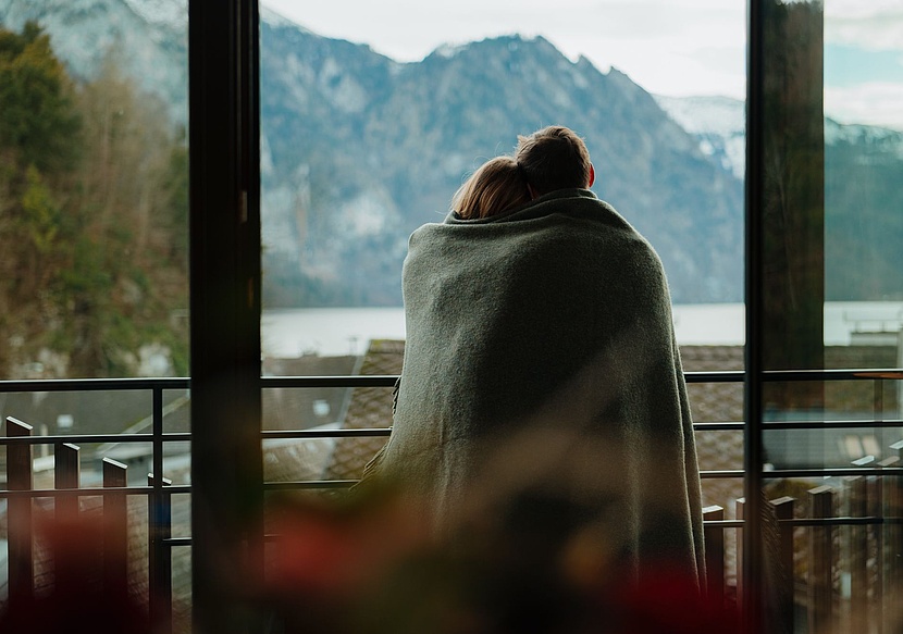 Paar in Decke gehüllt, das vom Zimmer aus den Blick auf Berge und See genießt.