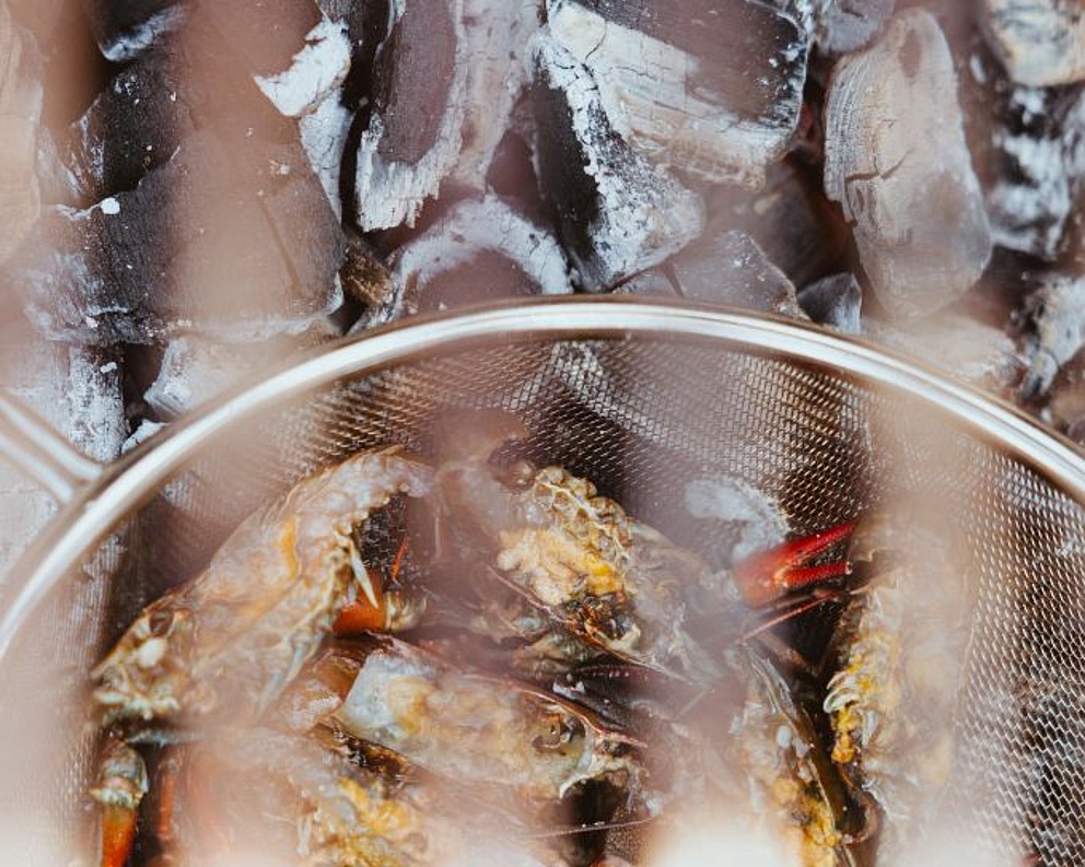 Fische in einem Metallsieb über glühender Holzkohle