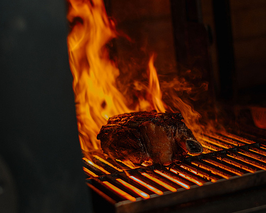 Dunkles Bild mit Feuer, auf dem Grillrost liegendem Fleisch