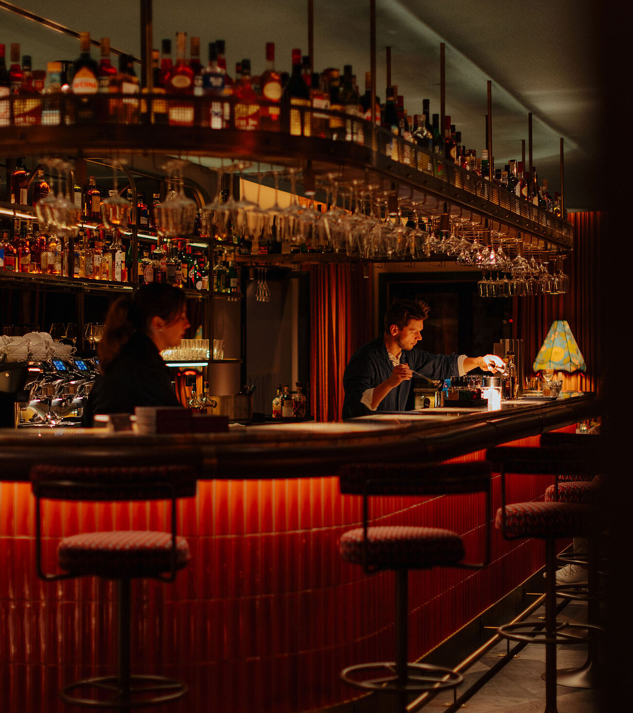 Der Barbereich mit gemütlichen Barstühlen, einer gut bestückten Bar und einem Barkeeper, der Getränke zubereitet
