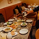 Einladender Restaurantbereich mit Gästen, während Wein in Gläser eingeschenkt wird. Verschiedene Speisen sind auf dem Tisch angerichtet.