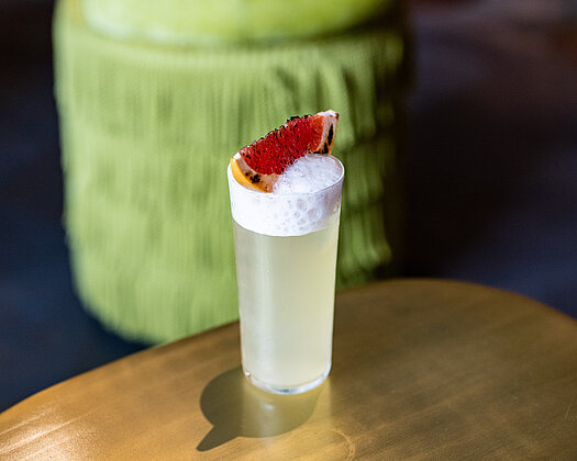 Verveine-Cocktail mit Blutorange auf braunem Tisch in der Beletage, im Hintergrund ein hellgrüner Hocker