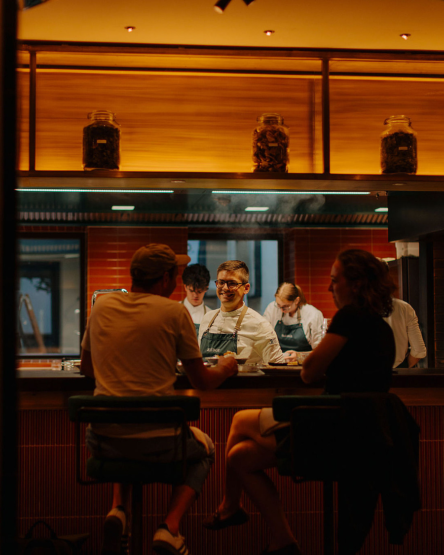 Offene Küche im Restaurant Beletage mit Köchen bei der Zubereitung. Gäste sitzen am Counter und beobachten das Geschehen
