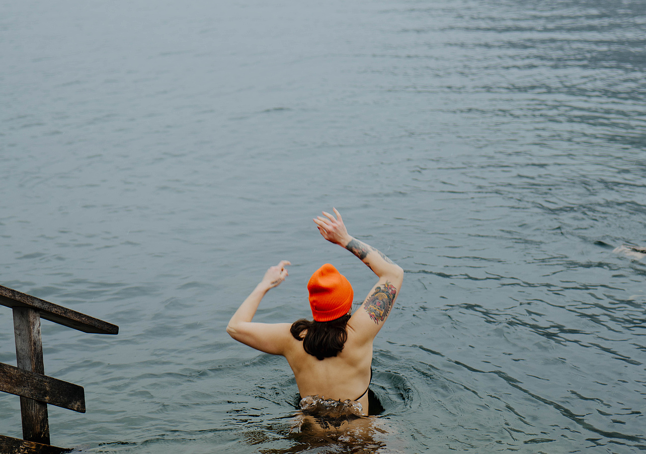 Frau im Bikini und orangefarbenen Mütze, die in den Traunsee zum Eisbaden geht