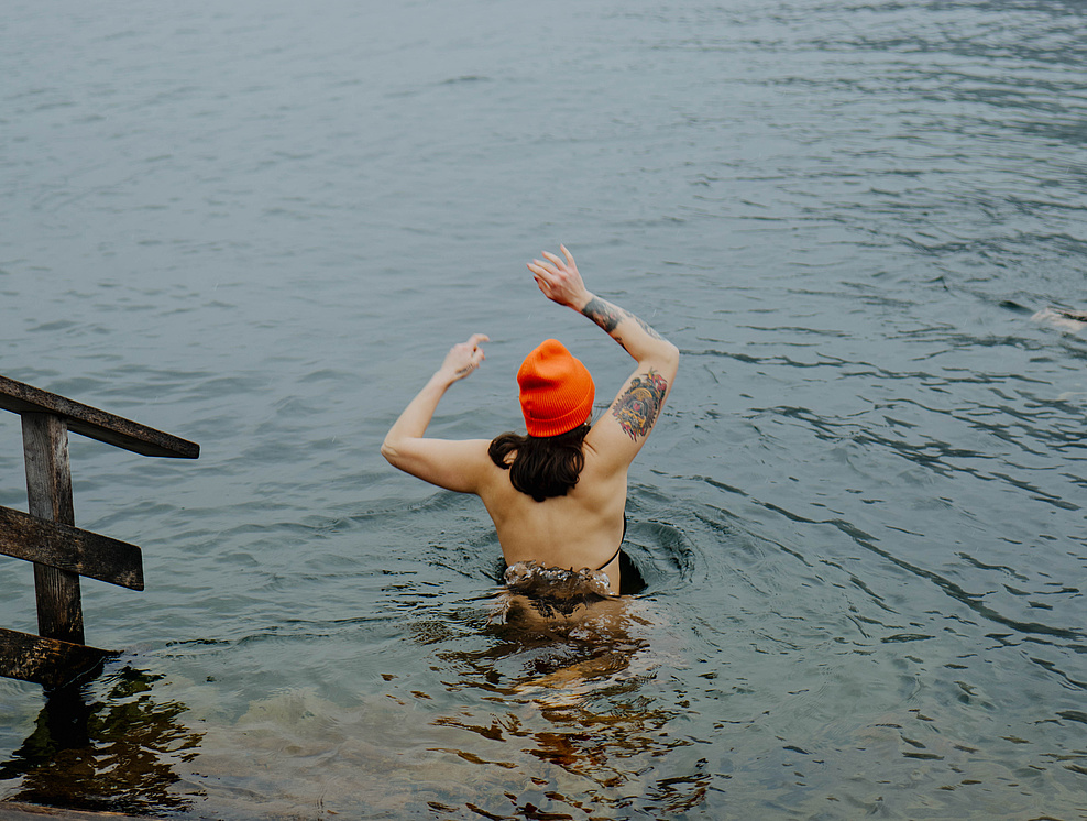 Frau im Bikini und orangefarbenen Mütze, die in den Traunsee zum Eisbaden geht