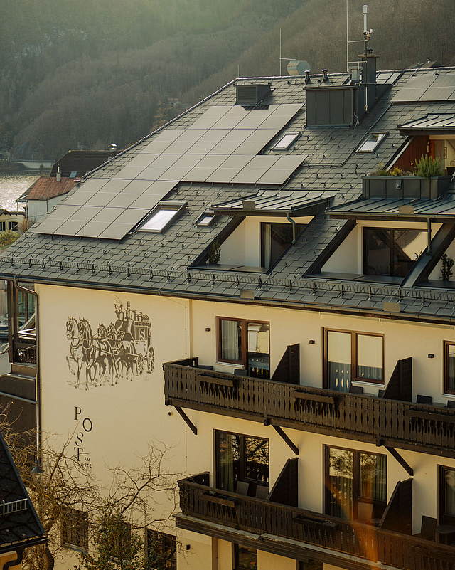 Seitenansicht des Hotels mit Balkonen und Logo an der Hauswand, im Hintergrund Berge und der Traunsee in der Ferne