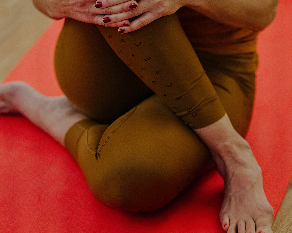 Person in sitzender Yogapose auf einer roten Matte