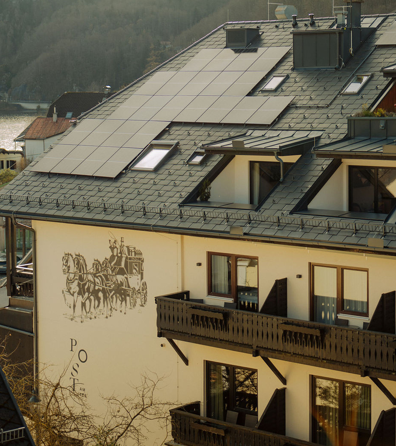 Seitenansicht des Hotels mit Balkonen und Logo an der Hauswand, im Hintergrund Berge und der Traunsee in der Ferne