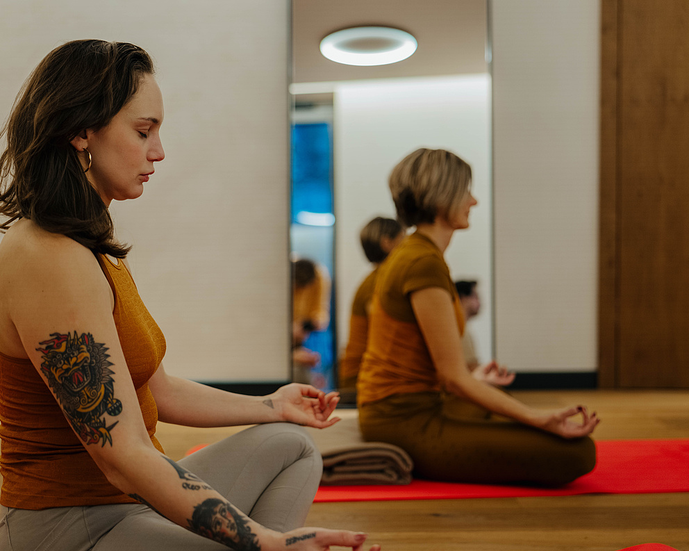 Seitliche Ansicht der Teilnehmer in einer Yogasession, sitzend mit Spiegel im Hintergrund