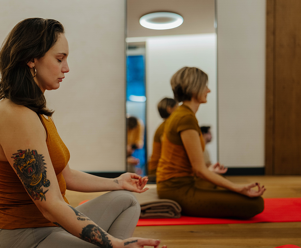 Seitliche Ansicht der Teilnehmer in einer Yogasession, sitzend mit Spiegel im Hintergrund