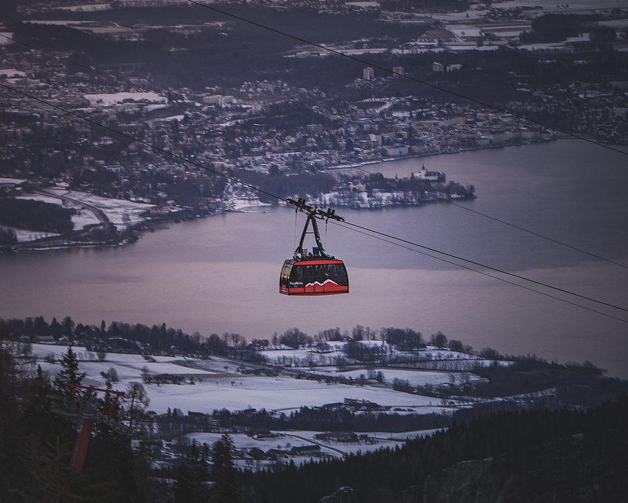 Rote Seilbahnkabine auf dem Weg zur Bergstation am Feuerkogel, mit Blick auf den winterlichen Traunsee und Gmunden im Abendlicht