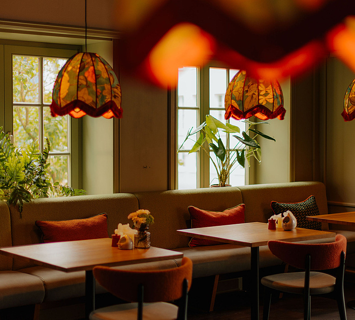 Gemütlicher Restaurantbereich mit braunen Tischen und bunten Lampenschirmen in herbstlichen, warmen Tönen.