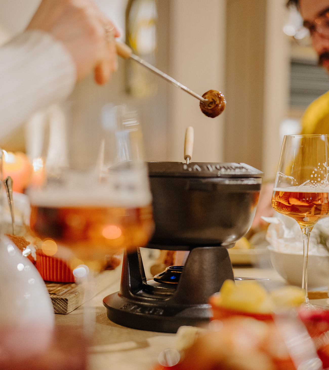 Fondue im Mittelpunkt mit zwei Weingläsern, Vordergrund leicht verschwommen
