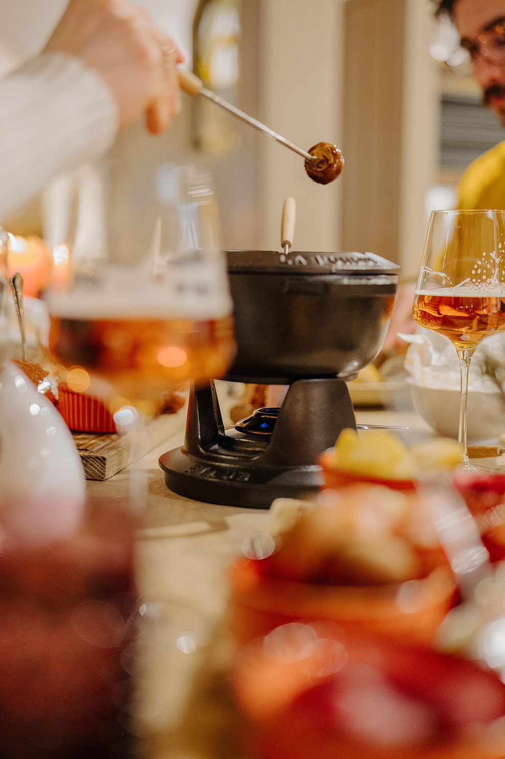 Fondue im Mittelpunkt mit zwei Weingläsern, Vordergrund leicht verschwommen