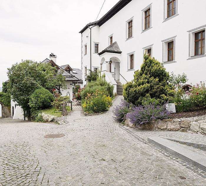 Außenansicht des historischen Klostersaals in Traunkirchen mit gepflastertem Zugang, Garten und Blick Richtung Traunsee.