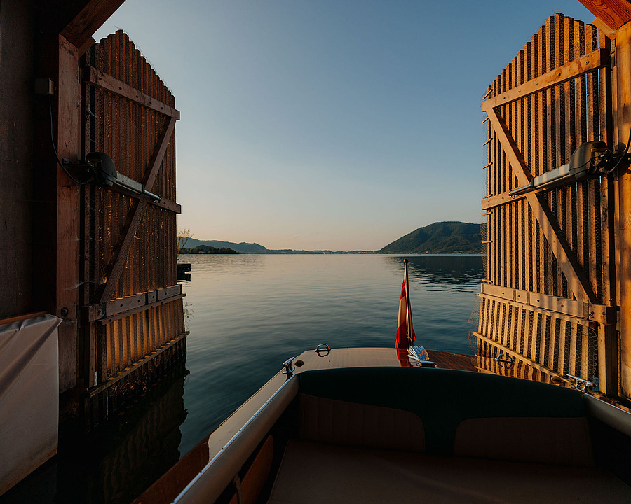Boot auf dem Traunsee fährt durch ein Holztor, warmes Sonnenlicht.
